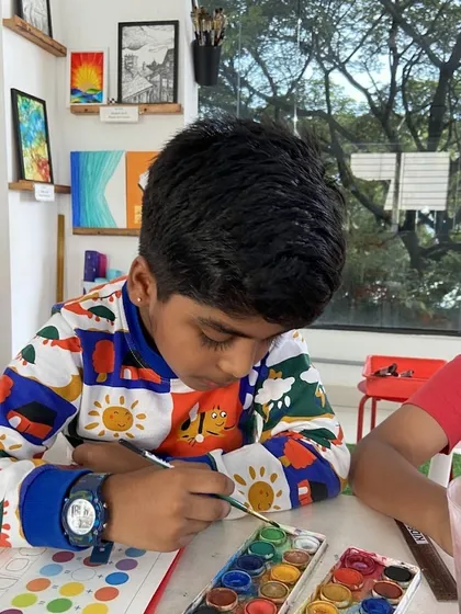 A young student in our kids' class is focused on his watercolor painting. We introduce children to a variety of mediums, like this watercolor set, to help them discover different techniques and find what they enjoy most.