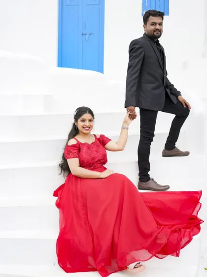 A classic pose on the steps of our Santorini-themed location. The bride's red gown and the groom's holding her hand create a timeless romantic photo.