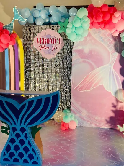 A vibrant Mermaid theme setup with a custom-shaped mermaid tail table and a colorful balloon arch against a shimmer backdrop.