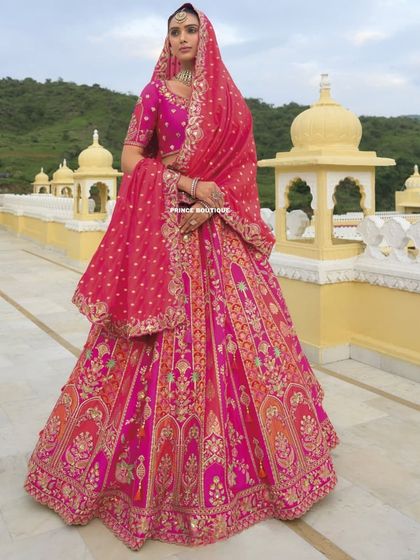 This royal pink and orange bridal lehenga is a masterpiece of color and craftsmanship. The full skirt features detailed embroidery depicting traditional motifs, perfect for a grand wedding.