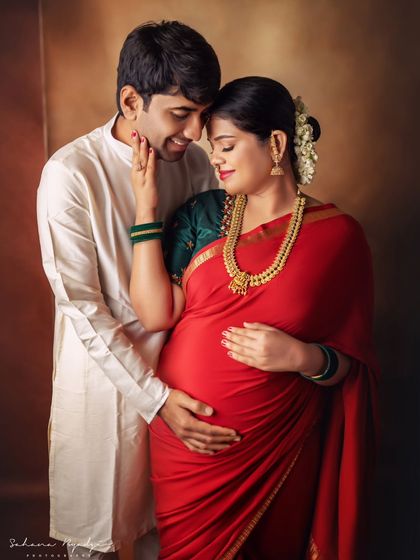 A tender moment between partners. The way he gently holds her as she cradles her bump speaks volumes about their shared love and anticipation. A perfect couple portrait in traditional wear.