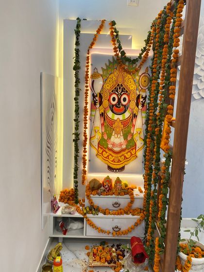 A beautiful mandir setup for a housewarming ceremony, featuring a large, backlit portrait of Lord Jagannath and a low-height console with drawers.