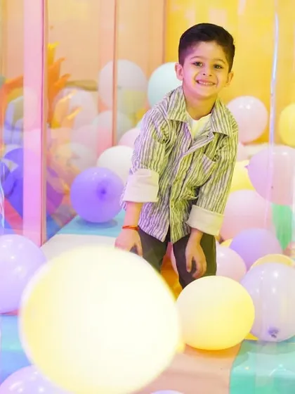 A smiling boy surrounded by balloons in one of our transparent play cubes during a fairy garden party.