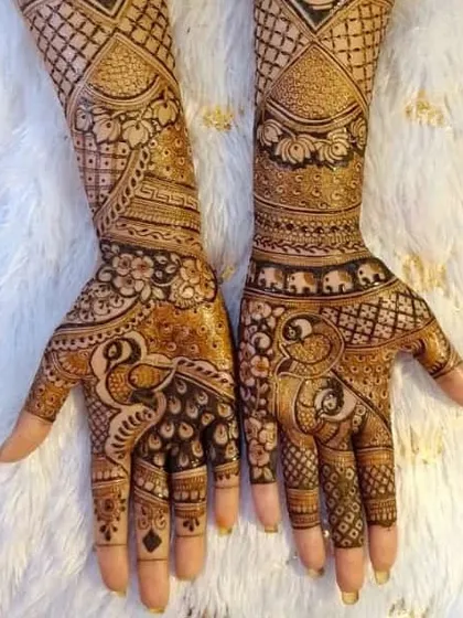 A classic bridal design with peacocks on the palms and elephants on the wrists, set against a soft, furry background that makes the henna details stand out.