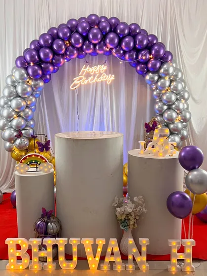Another view of the purple and silver themed birthday decoration for Bhuvan. The lighting on the balloons and marquee letters creates a vibrant atmosphere for the celebration.