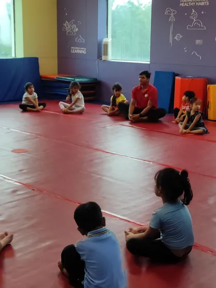 A full house for circle time. A coach leads a group of children in seated stretches, an important part of warming up and cooling down.