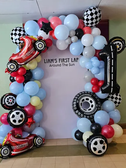 "Liam's First Lap Around The Sun" race car themed balloon arch. This photo booth frame is decorated with car and tire-shaped foil balloons and checkered flag details.