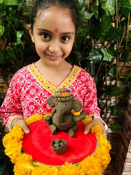 A sweet smile from a student holding her clay Ganesha, adorned with a colorful paper hat.