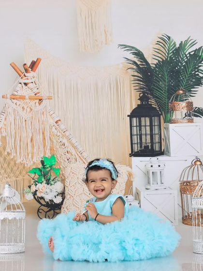 A happy baby girl in a blue dress, surrounded by boho-chic decor. The teepee, lanterns, and birdcages create a magical and enchanting atmosphere for her portrait session.