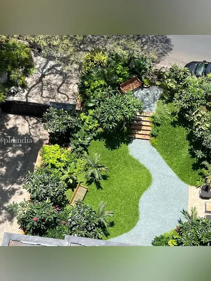 An aerial view of an entrance garden in South Mumbai. The design features a meandering gravel path, undulating lawns, and multiple seating areas, making it a functional and beautiful communal space.