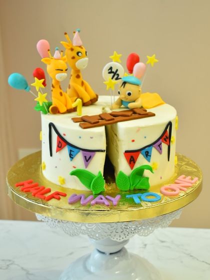 Celebrating a sweet milestone with this "Halfway to One" cake. This adorable design for a 6-month celebration features cute giraffes, a baby figurine, and colorful party details.