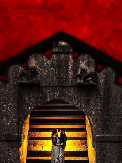 A creative frame-within-a-frame shot at a historic fort. The dramatic red and the ancient stone archway create a powerful, artistic, and unforgettable pre-wedding image.