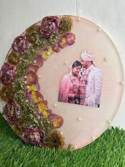 A round varmala preservation frame, featuring a wedding photo surrounded by the couple's preserved garlands and delicate pearls.