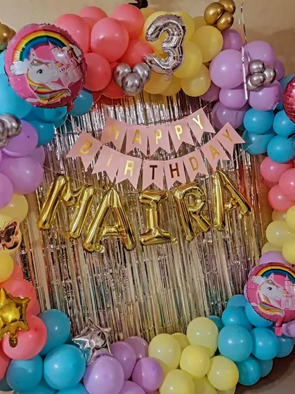 A close-up of the 'Happy Birthday' banner and the name 'Maira' in gold foil balloons, part of the unicorn theme setup.