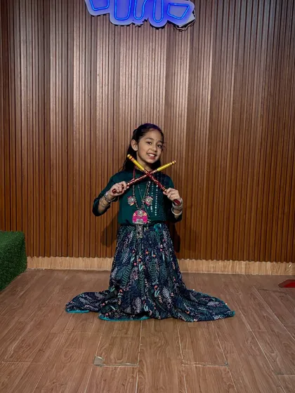 A happy dancer kneels for a photo, showcasing her beautiful printed skirt and dandiya. We make sure every child feels like a star in our studio.