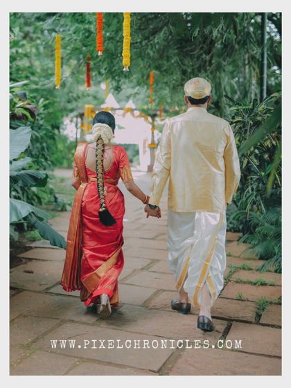 The journey begins. A simple, beautiful shot of the couple walking hand-in-hand, showcasing the bride's traditional hairstyle and the groom's classic veshti.