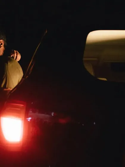 A quiet, intimate moment in the back of a car at night. The red taillight casts a soft glow on the couple as they embrace, creating a feeling of being in their own private world.