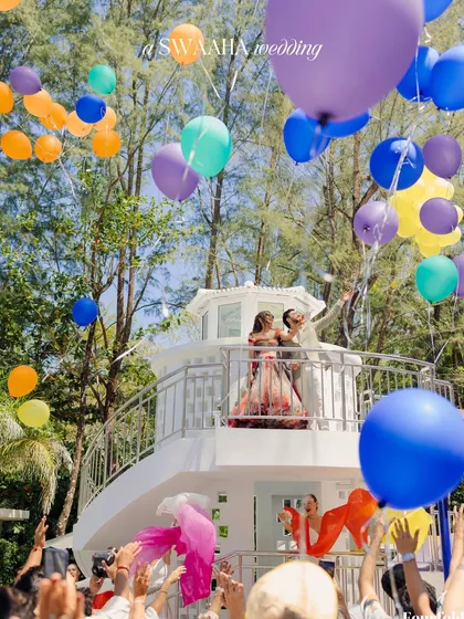 A joyful moment as the couple releases a cascade of colorful balloons from a white balcony, a perfect photo opportunity.