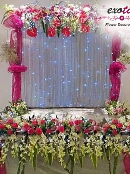 A beautiful puja backdrop with a curtain of fairy lights. The stage is adorned with a mix of pink and white flowers, creating a sparkling and divine effect.