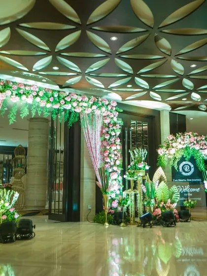 This entrance is a celebration of texture and color, with pink floral arches, gold birdcage-like structures, and large, artistic green leaves creating a unique and vibrant welcome.