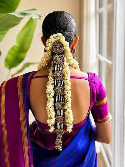 The hairstyle for this look featured an elaborate 'jada' or hair extension, adorned with flowers and silver jewelry, which is a classic element of South Indian bridal styling.