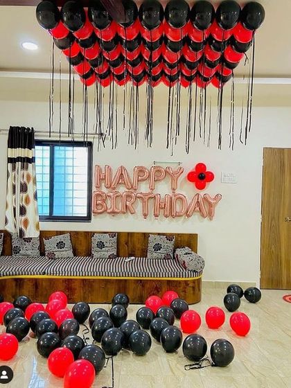 A simple and bold living room decoration with red and black balloons. The setup includes balloons on the ceiling and a rose gold "Happy Birthday" foil banner.