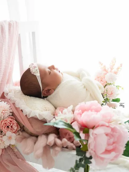 A side view of the floral setup, showcasing the delicate profile of the sleeping newborn against the soft pink peonies.