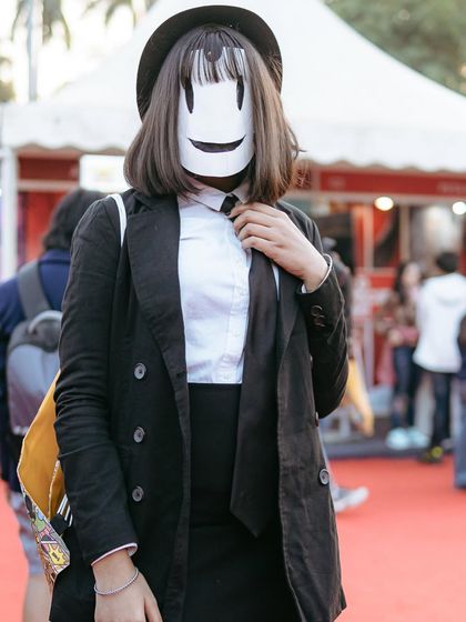 A cosplayer as Sniper Mask from High-Rise Invasion, striking a pose that captures the character's mysterious vibe. The mask and formal attire are perfectly executed.