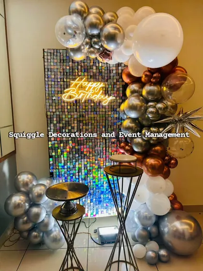 This modern and chic birthday setup features a dazzling holographic shimmer wall that catches the light beautifully. It's complemented by a custom 'Happy Birthday' neon sign and a stylish chrome and copper balloon garland.