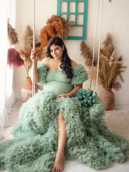 A full-length portrait featuring a mint green ruffled gown. The studio swing and boho-chic pampas grass decor add a touch of whimsy to this elegant shot.
