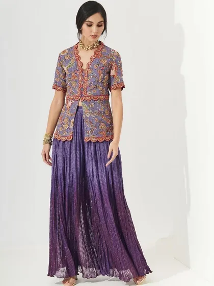 A model in a beautiful purple sharara set with a floral jacket. The makeup is soft and fresh, with a clean base and a hint of color on the lips, perfect for a daytime wedding event.