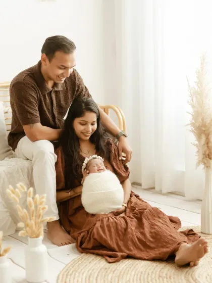 A relaxed family portrait in our light-filled studio. The mother holds the baby while the father looks on, surrounded by our signature boho decor.