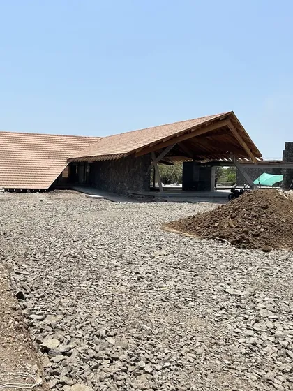 A wider view of the Alibaug residence site. The building's low-slung form and natural material palette of wood, stone, and tile help it settle gently into the flat, coastal landscape.