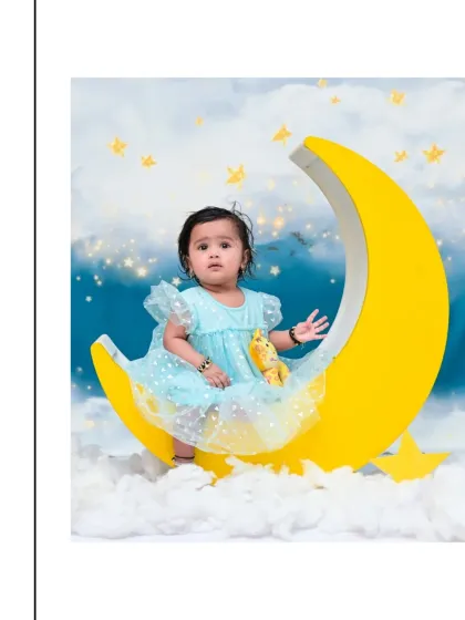 A sweet baby girl in a light blue dress sits on a crescent moon prop. This dreamy moon-themed photoshoot is perfect for capturing the quiet and gentle moments of babyhood.