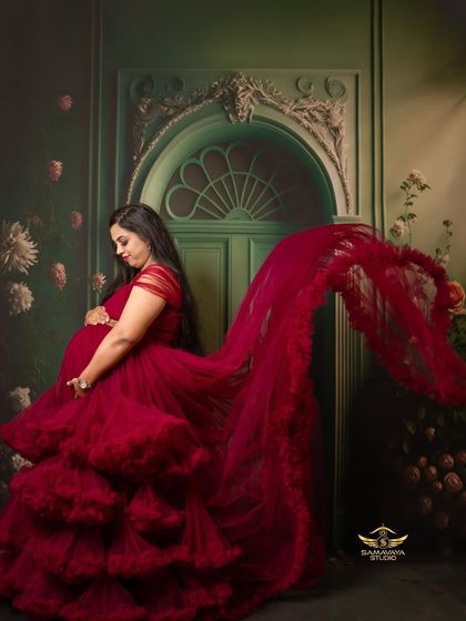 A profile view of the magnificent red gown, showing its flowing trail and rich texture against a painterly green backdrop.