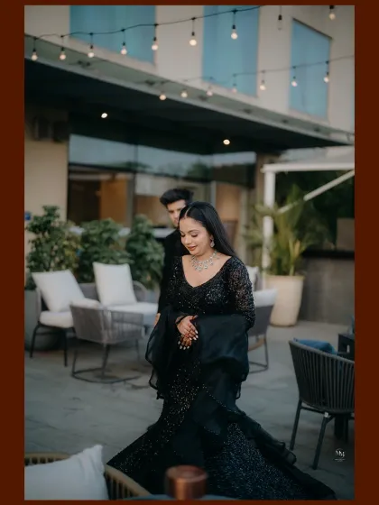 A wide shot capturing the couple at their outdoor reception venue. The elegant black attire and sophisticated setting create a luxurious feel.