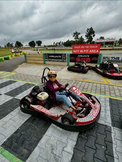 A racer poses in the pit lane, ready to hit the track. The checkered floor and lineup of karts set the scene for the action to come.