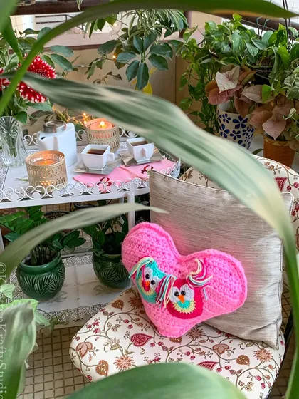 The Valentine's heart cushion, styled in a cozy balcony setting. It adds a perfect pop of pink and a feeling of warmth to this little outdoor retreat.