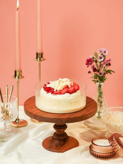 A full view of the Strawberry Vanilla Tres Leches, elegantly presented on a wooden cake stand.