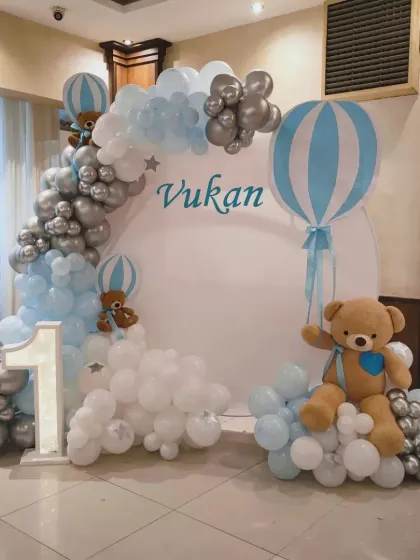 A hot-air balloon and teddy bear theme for Vukan's first birthday, using a soft blue, white, and silver palette.