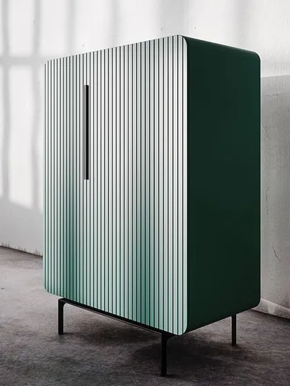 The fluted cabinet shown in a deep green, with its gentle curves and minimalist black metal handle and legs.