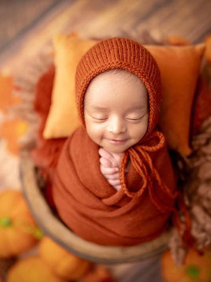 A smiling newborn surrounded by pumpkins and autumn colors. This seasonal setup is a fun way to celebrate an autumn baby.