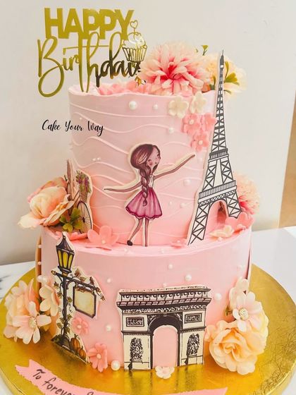 A little Paris, a lot of sweetness. This two-tier pink cake is decorated with iconic Parisian landmarks for a travel-themed birthday.