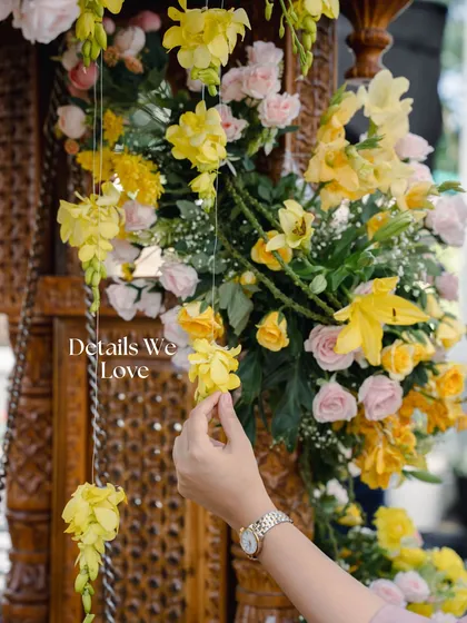 A close-up of the floral details from the greenhouse Haldi. My hand adjusts a delicate string of yellow flowers, showcasing the care that goes into every single element of the decor.