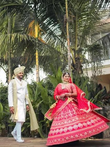 The bride twirls in her stunning red lehenga while her groom watches with a smile, a beautiful, dynamic shot full of life.