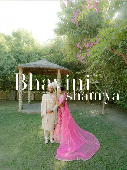 A stunning wide-angle shot of the couple in the garden, the bride's long pink veil creating a dramatic and beautiful effect.