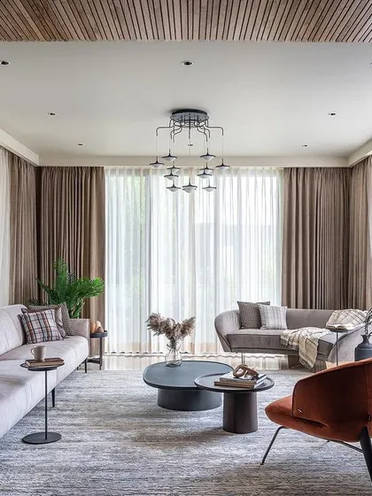 This living room demonstrates a clean, contemporary aesthetic with a touch of warmth. I balanced the neutral tones of the sofas and drapes with a pop of burnt orange in the armchair and a slatted wood ceiling, creating a sophisticated yet inviting residential space.