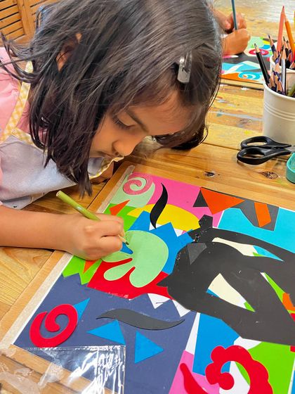 A student carefully adds details to her Henri Matisse-inspired cut-out collage, learning about organic shapes and vibrant color combinations.