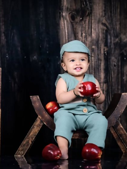 A baby boy in a cute outfit holding an apple.