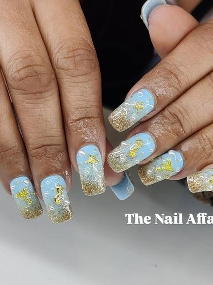 A fun, under-the-sea themed design on square nails, with a blue and gold glitter base and 3D seashell, starfish, and pearl embellishments.